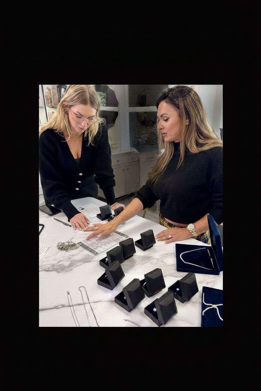 Two women at a table reviewing diamond jewelry laid out on display stands.