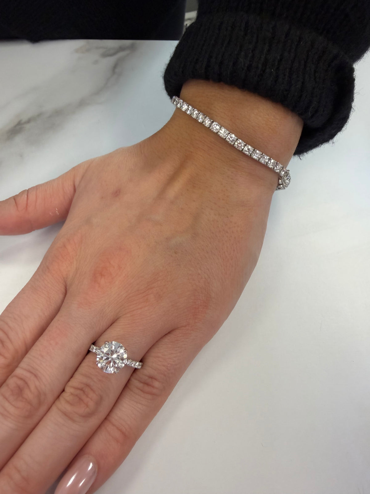 A round solitaire diamond engagement ring and diamond tennis bracelet worn together.